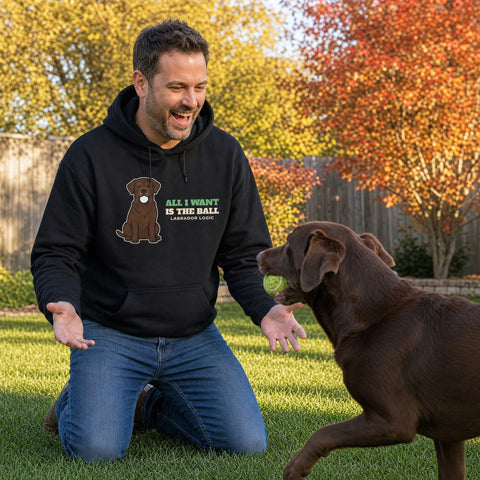 Man laughing in a black All I Want Is the Ball labrador hoodie as his chocolate lab brings a tennis ball - funny lab dad gift