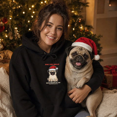 Pug mom in a black Pug the Halls Christmas hoodie hugging her pug in a Santa hat by the Christmas tree - funny pug Christmas gift