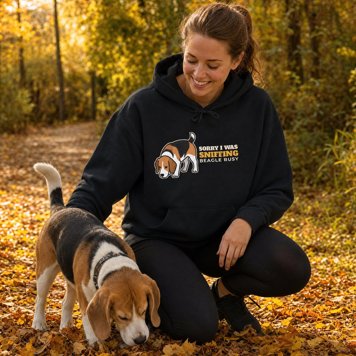 Woman in a black Sorry I Was Sniffing beagle hoodie kneeling beside her beagle on an autumn trail - funny beagle mom gift