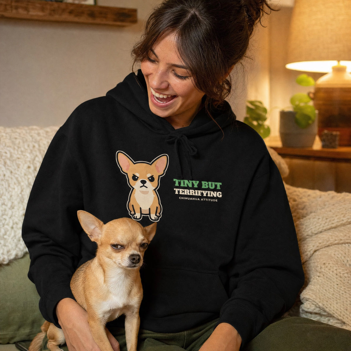 Woman laughing in a black Tiny But Terrifying chihuahua hoodie with her grumpy chihuahua on her lap - funny chihuahua mom gift
