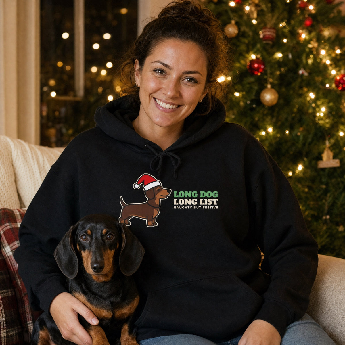 Woman wearing a black dachshund Christmas hoodie with a Santa hat wiener dog, cuddling her dachshund by the tree - funny dog mom gift