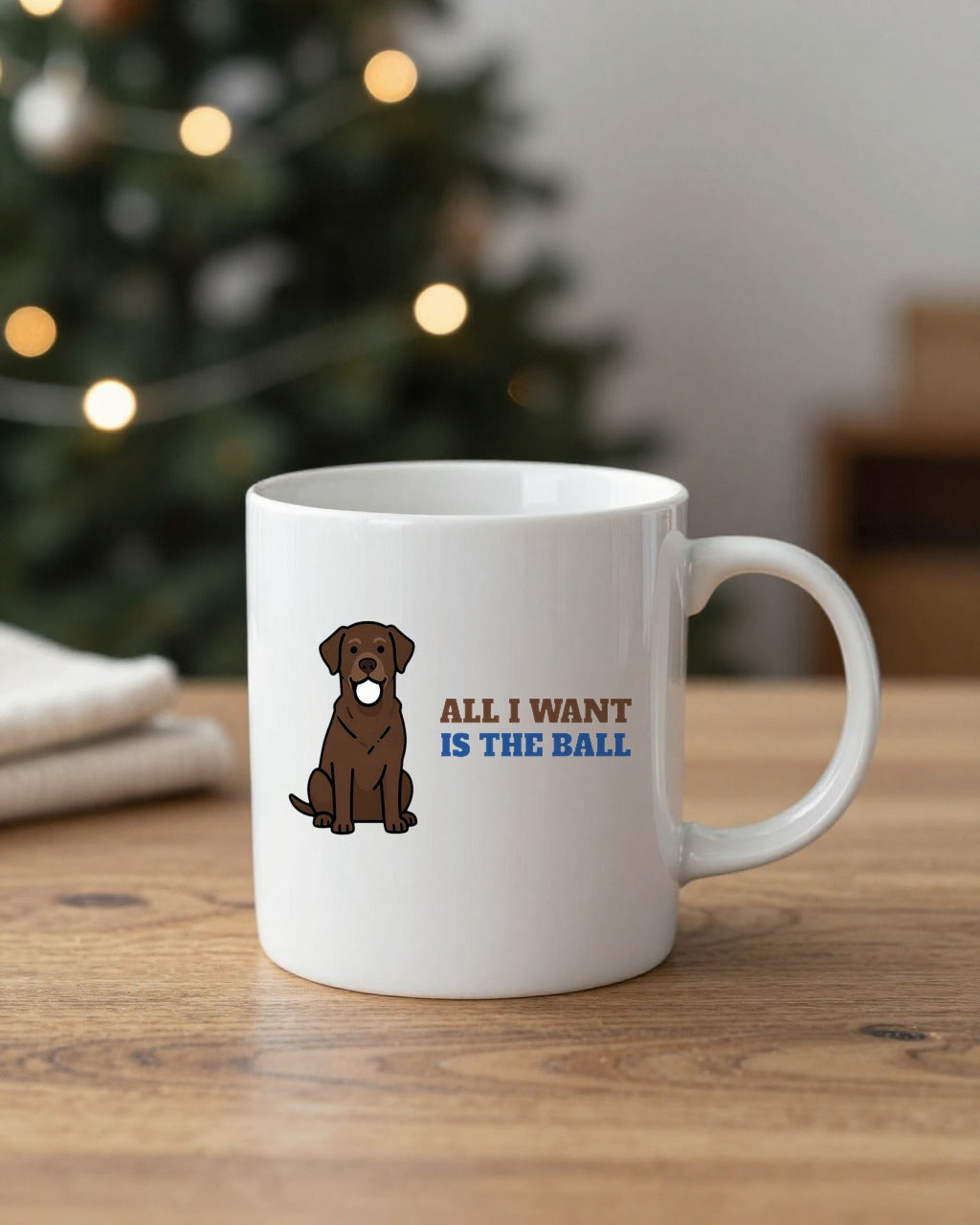 All I Want Is the Ball Labrador mug on a table by a Christmas tree