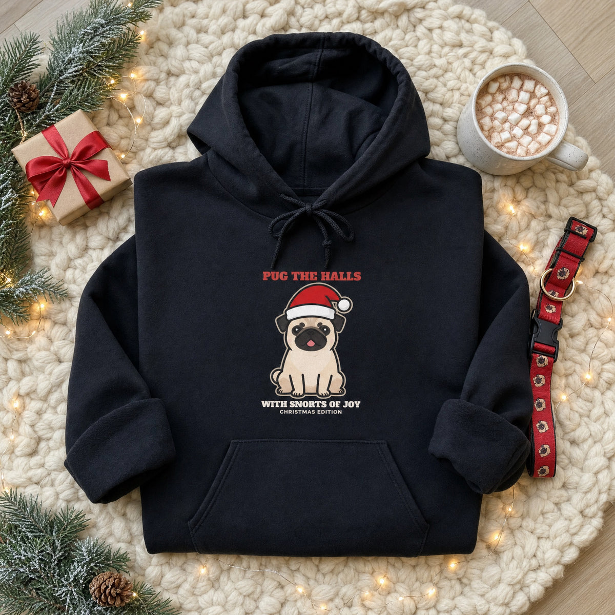 Black pug Christmas hoodie with Santa hat pug design folded on a cozy knit blanket with Christmas lights