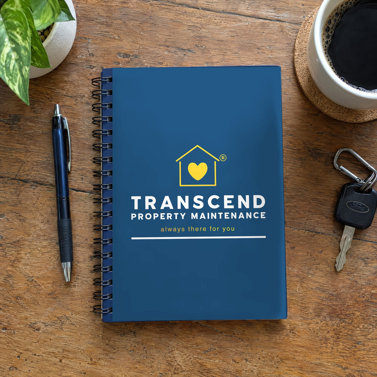 Transcend Property Maintenance spiral notebook on a desk with a pen and truck keys (AI-generated example scene, cover artwork placed from the real design)