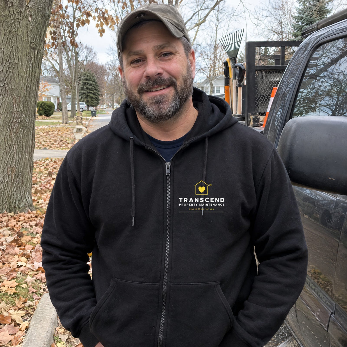 Landscaper wearing the Transcend Property Maintenance black full-zip hoodie with the logo on the left chest (AI-generated example photo, logo placement matched to the real product)